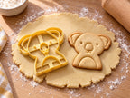 Butter-gelber Koala-Ausstecher mit Prägung neben gebackenem Keks mit flauschigen Ohren, großer Nase und Bäuchlein auf hellem Holz