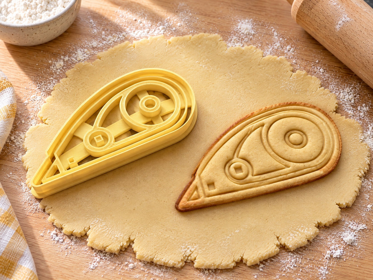 Butter-gelber Korrekturroller-Ausstecher mit Prägung neben gebackenem Keks mit zwei Spulen und schmaler Spitze auf hellem Holz