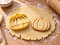 Butter-gelber Kürbis-Ausstecher mit Prägung neben breitem Kürbis-Keks mit fünf glatten Rippen und geradem Stiel auf hellem Holz