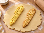 Butter-gelber Kugelschreiber-Ausstecher mit Prägung neben schmalem gebackenem Keks mit Clip und Druckknopf auf hellem Holz