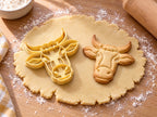 Butter-gelber Kuhkopf-Ausstecher mit Prägung neben gebackenem Keks mit Hörnern, Ohren und breitem Maul auf hellem Holz