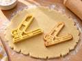 Butter-gelber Locher-Ausstecher mit Prägung neben gebackenem Keks mit schrägem Hebel und runden Stanzen auf hellem Holz