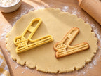 Butter-gelber Locher-Ausstecher mit Prägung neben gebackenem Keks mit schrägem Hebel und runden Stanzen auf hellem Holz