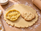Butter-gelber Malteser-Ausstecher mit Prägung neben gebackenem Keks mit Knopfaugen und weichem Fellrahmen auf hellem Holz
