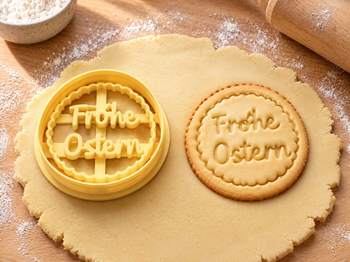 Butter-gelber Medaillon-Ausstecher mit Prägung neben ovalem Keks mit Wellenrand und Schriftzug Frohe Ostern auf hellem Holz