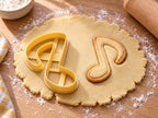 Butter-gelber Musiknoten-Ausstecher neben gebackener Achtelnote als Keks mit Fähnchen und glatter Fläche auf hellem Holz