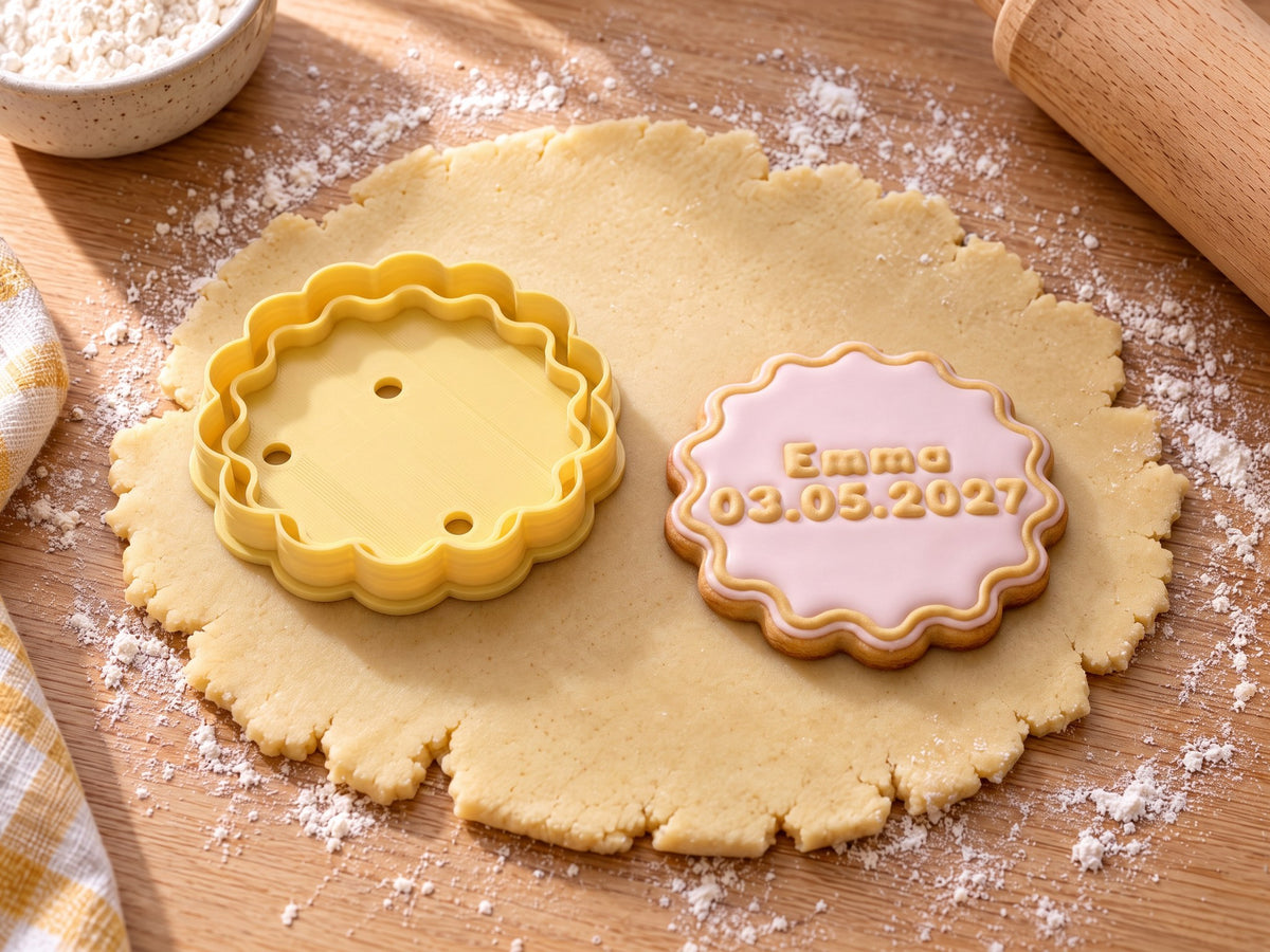 Butter-gelber Wellenkreis-Ausstecher neben gebackenem Keks mit Wellenrand, rosa Zuckerguss und geprägtem Text „Emma 03.05.2027“ auf ausgerolltem Teig und hellem Holz