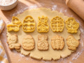 Set Ostern: 5 butter-gelbe Ausstecher mit Prägung nebeneinander mit gebackenen, geprägten Keksen auf ausgerolltem Teig und hellem Holz