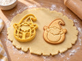 Butter-gelber Osterwichtel-Ausstecher mit Prägung neben Keks mit Wichtel im Ei, Zipfelmütze und erhobenen Armen auf hellem Holz