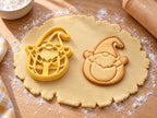 Butter-gelber Osterwichtel-Ausstecher mit Prägung neben Keks mit Wichtel im Ei, Zipfelmütze und erhobenen Armen auf hellem Holz