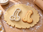 Penis gebogen-Ausstecher mit Prägung neben gebackenem Keks auf hellem Holz