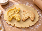 Butter-gelber Pferdekopf-Ausstecher mit Prägung neben gebackenem Keks mit Profil, fließender Mähne und Nüstern auf hellem Holz