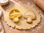 Butter-gelber Pilz-Ausstecher mit Prägung neben gebackenem Keks mit hohem Glockenhut und Lamellen auf hellem Holz