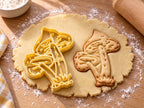 Butter-gelber Ausstecher mit Prägung: zwei Pilze im Grasbüschel, daneben gebackener Keks mit gesprenkelten Hüten auf hellem Holz