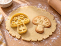 Butter-gelber Pilz-Ausstecher mit Prägung neben gebackenem Keks mit fünf runden Tupfen auf dem Hut auf hellem Holz