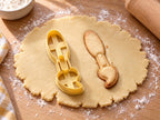 Butter-gelber Pinsel-Ausstecher mit Prägung neben gebackenem Keks mit rundem Stiel und geschwungenen Borsten auf hellem Holz