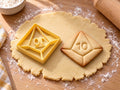 Butter-gelber Ausstecher mit Prägung als Zehnseiter-Würfel neben gebackenem Keks mit Kantenlinien und der Zahl 10 auf hellem Holz