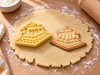 Butter-gelber Schachbrett-Ausstecher mit Prägung neben gebackenem Keks mit kariertem Brett und Figurenreihe auf hellem Holz