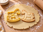 Butter-gelber Schaukelpferd-Ausstecher mit Prägung neben Keks mit Mähne, Sattel und Kufe auf hellem Holz