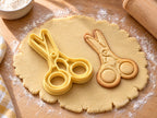 Butter-gelber Scheren-Ausstecher mit Prägung neben gebackenem Keks mit runden Griffen und Gelenkschraube auf hellem Holz