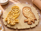 Butter-gelber Schleiereulen-Ausstecher mit Prägung neben gebackenem Keks mit herzförmigem Gesicht und Federzeichnung auf hellem Holz