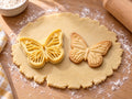 Butter-gelber Schmetterling-Ausstecher mit Prägung neben gebackenem Keks mit fein geäderten Flügeln und Fühlern auf hellem Holz