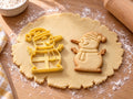 Butter-gelber Schneemann-Ausstecher mit Prägung neben gebackenem Keks mit langer Karottennase, Pudelmütze und Zweigarmen auf hellem Holz