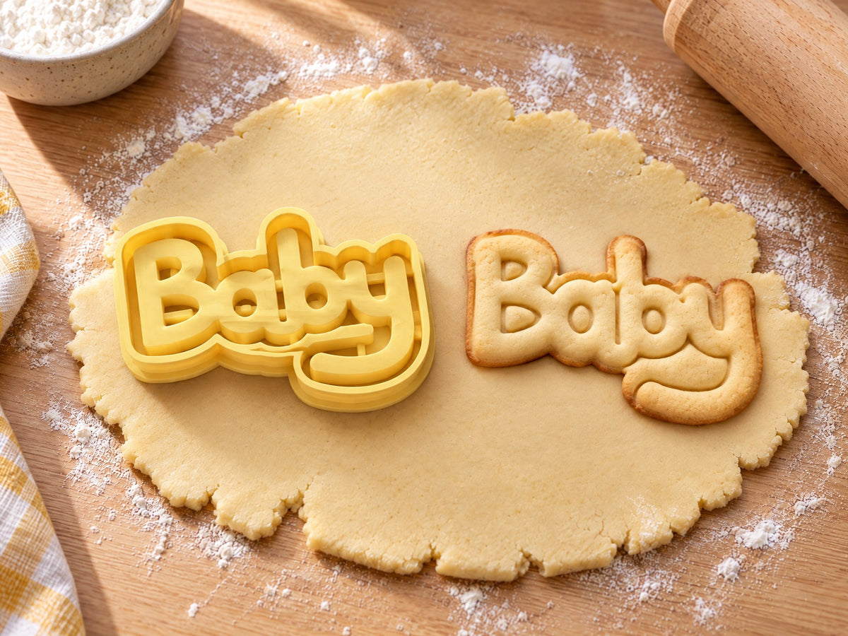 Butter-gelber Baby-Ausstecher mit Prägung neben Keks mit rundem Schriftzug „Baby“ und geschwungenem y auf hellem Holz