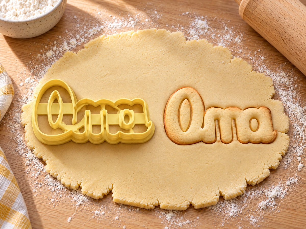 Butter-gelber Oma-Ausstecher mit Prägung neben Keks mit verbundenem Schreibschrift-Schriftzug „Oma“ auf hellem Holz