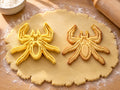 Butter-gelber Spinnen-Ausstecher mit Prägung neben schlankem Spinnen-Keks mit langen, geknickten Beinen auf hellem Holz