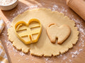 Butter-gelber Tassenrand-Ausstecher mit Prägung in Herzform neben gebackenem Keks in Herzform mit Glanzbogen und Schlitz auf hellem Holz