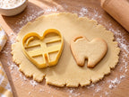 Butter-gelber Tassenrand-Ausstecher mit Prägung in Herzform neben gebackenem Keks in Herzform mit Glanzbogen und Schlitz auf hellem Holz
