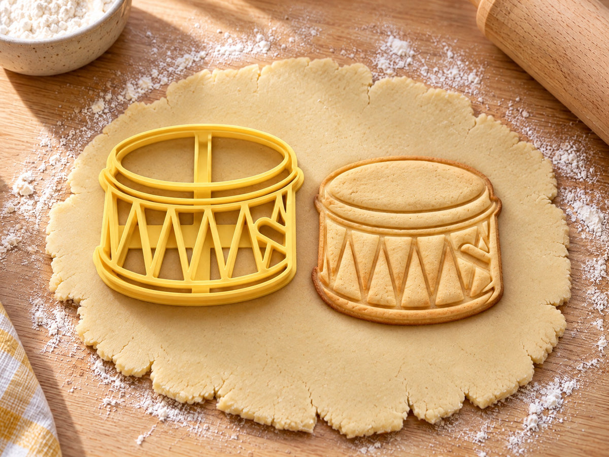 Butter-gelber Trommel-Ausstecher mit Prägung neben gebackenem Keks mit Zickzack-Schnur und Dreiecksfeldern am Kessel auf hellem Holz