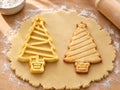 Butter-gelber Weihnachtsbaum-Ausstecher mit Prägung neben gebackenem Keks mit Schrägstreifen und Baum im Kübel auf hellem Holz