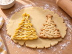Butter-gelber Weihnachtsbaum-Ausstecher mit Prägung neben gebackenem Keks mit Stern, Perlengirlanden und Kugeln auf hellem Holz
