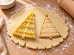Butter-gelber Weihnachtsbaum-Ausstecher mit Prägung neben gebackenem Keks mit Punktmuster und gewellten Etagen auf hellem Holz
