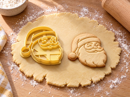 Weihnachtsmann-Ausstecher mit Prägung neben gebackenem Keks mit lachendem Gesicht im Halbprofil auf hellem Holz