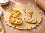 Butter-gelber Weihnachtssocken-Ausstecher mit Prägung neben gebackenem Keks mit Rautenbündchen und drei Bonbons auf hellem Holz
