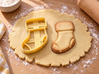 Butter-gelber Socken-Ausstecher mit Prägung neben gebackenem Keks mit breitem Umschlag, Ferse und Spitze auf hellem Holz