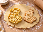 Butter-gelber Sockenpaar-Ausstecher mit Prägung neben gebackenem Keks mit zwei Socken im Schneeflocken-Strickmuster auf hellem Holz