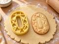 Butter-gelber Ausstecher Zahl 0 mit Prägung neben gebackenem ovalem Keks mit Rautenmuster auf hellem Holz