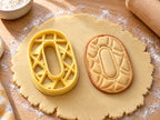 Butter-gelber Ausstecher Zahl 0 mit Prägung neben gebackenem ovalem Keks mit Rautenmuster auf hellem Holz