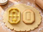 Butter-gelber Ausstecher Zahl 0 mit Prägung neben achteckigem Keks in Form einer Null mit Fenster auf hellem Holz