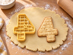Butter-gelber Ausstecher Zahl 4 mit Prägung neben gebackenem Keks mit Karo-Prägung und kleinem Dreieck auf hellem Holz