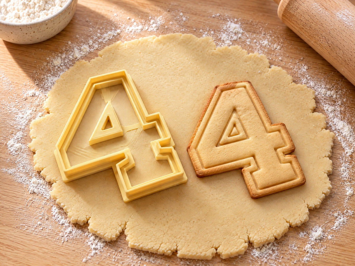 Butter-gelber Ausstecher Zahl 4 mit Prägung neben Keks in Form einer geschlossenen Vier mit doppelter Kontur auf hellem Holz