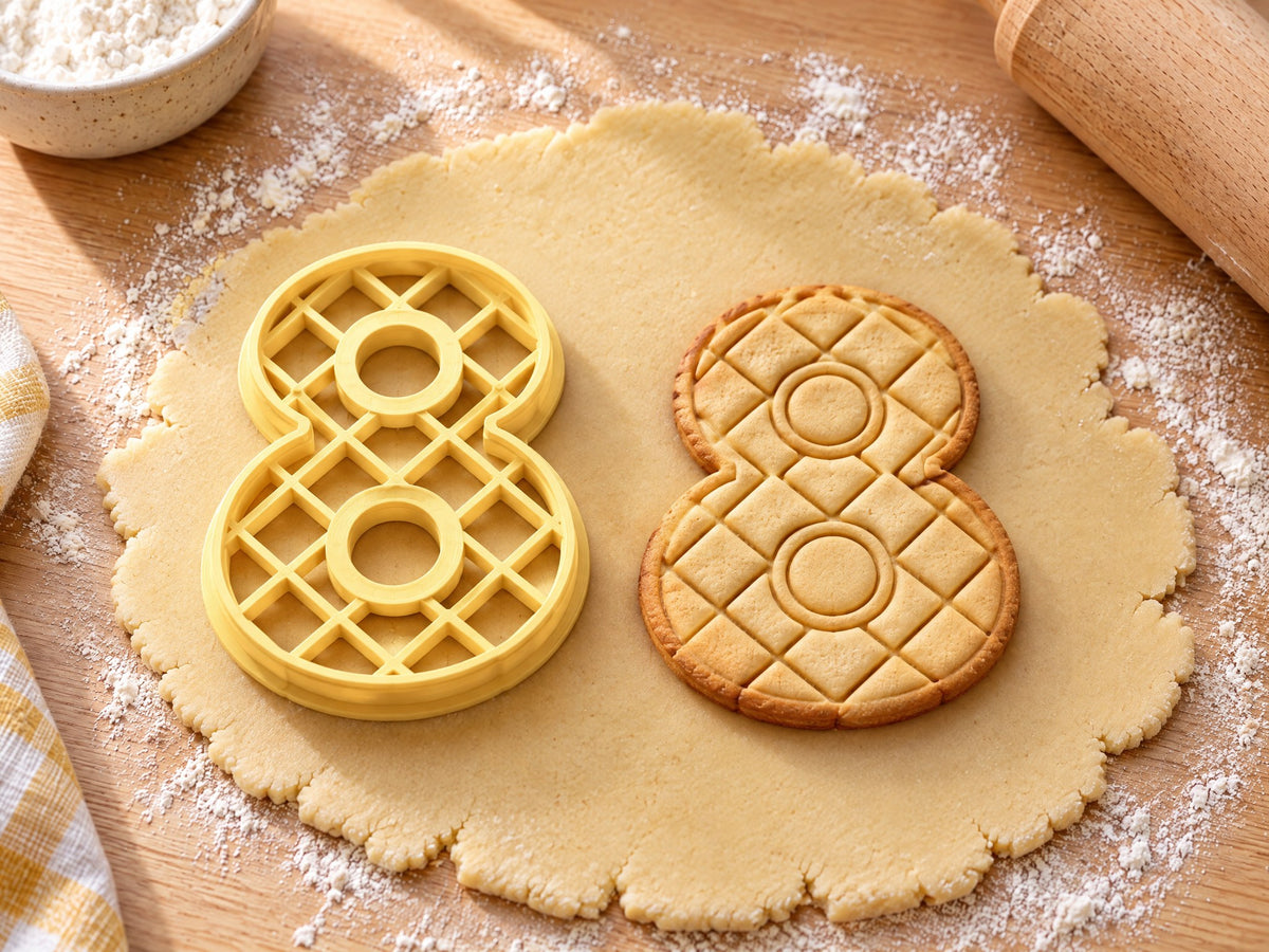 Butter-gelber Ausstecher Zahl 8 mit Prägung neben gebackenem Keks mit eingeprägtem Rautengitter auf hellem Holz