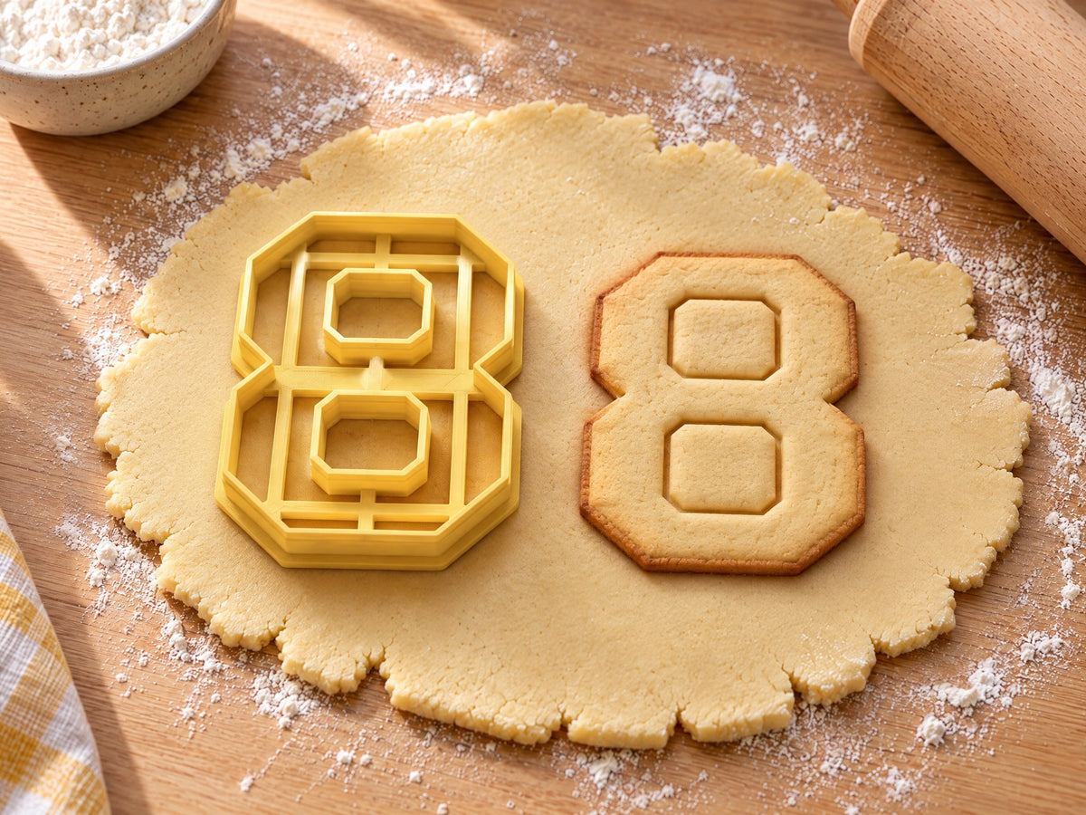 Butter-gelber Ausstecher Zahl 8 mit Prägung neben Keks in Form einer Acht mit zwei eckigen Fenstern auf hellem Holz