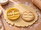 Butter-gelber Zahnspange-Ausstecher mit Prägung neben rundem Keks mit Schneidezähnen, Brackets und Draht auf hellem Holz