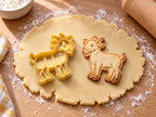 Butter-gelber Ziegen-Ausstecher mit Prägung neben gebackenem Keks mit Hörnern, Kinnbart und Stummelschwanz auf hellem Holz