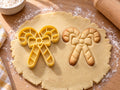 Butter-gelber Ausstecher mit Prägung neben gebackenem Keks mit zwei gekreuzten Zuckerstangen und Schleife auf hellem Holz